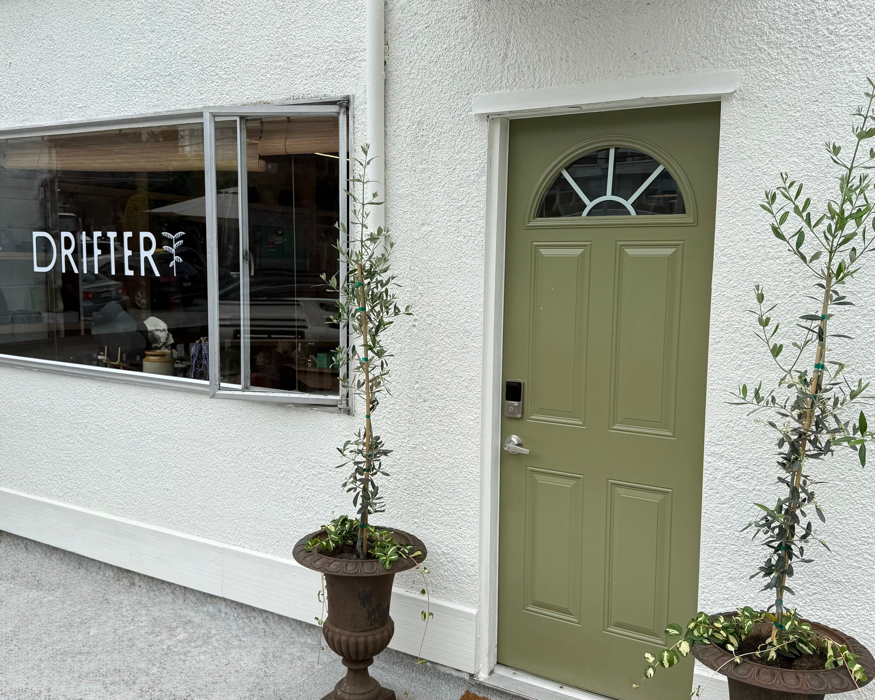 Front entrance of a building with a green door, striped awning, and potted plants.